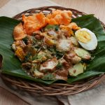 gado-gado is indonesian traditional food made of various steamed vegetables mixed with  spicy peanut sauce, rice cakes, egg and crackers served on wooden plate.